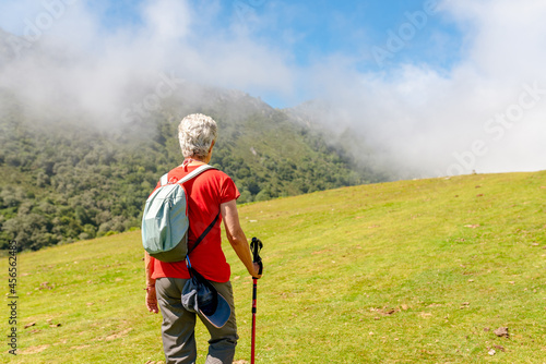 Elderly hiker walks across a hillside on a foggy sunny day.