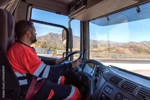 Truck driver in the driving position with both hands holding the steering wheel and driving.