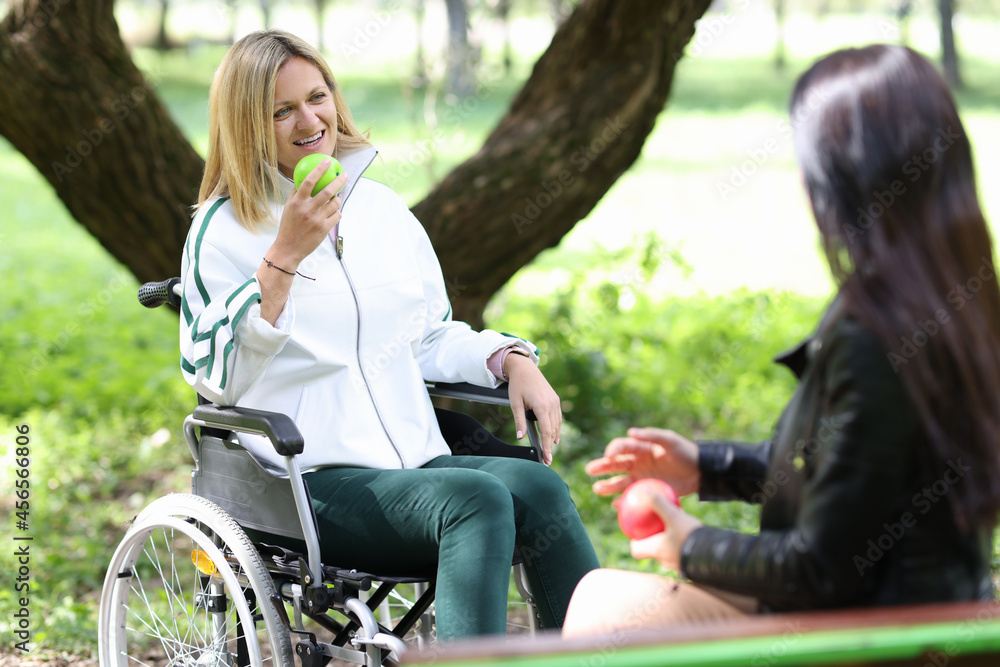 Disabled woman in wheelchair eating apple with her friend in park