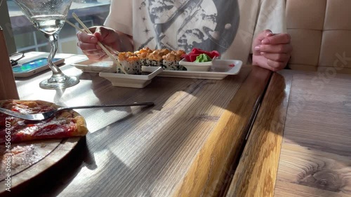 Dinner in sushi restaurant. Young woman eating Asian rolls on background. 4K. Japanese cuisine.