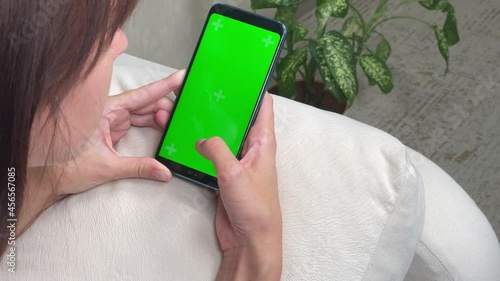 Woman schrolling Smartphone with Green Screen and Chroma Key with Tracking Markers. Comfort shopping. 4K. Plant on background.