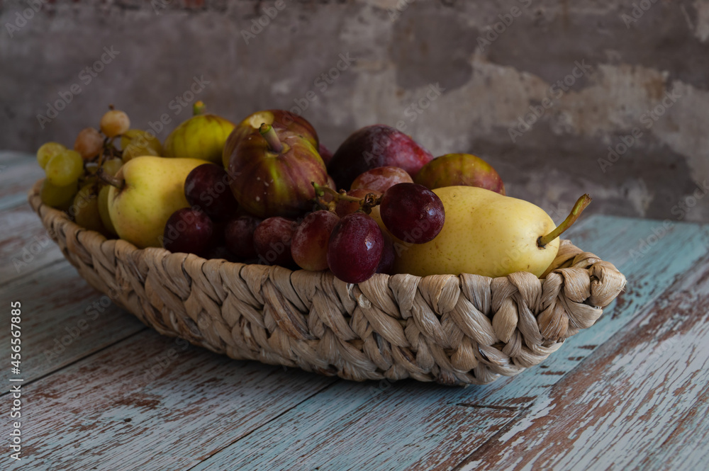 Still life with fruits pears and plums lie on a wicker plate in the form of a boat which stands on boards in the style of Provence against the wall