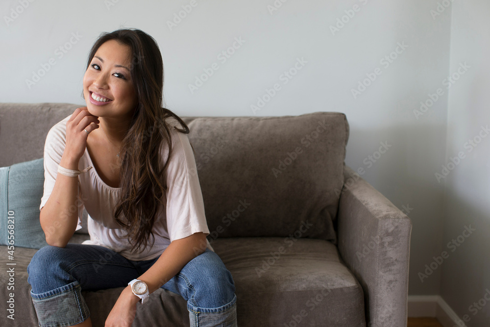 Obraz premium Young woman sitting on sofa with hand on chin
