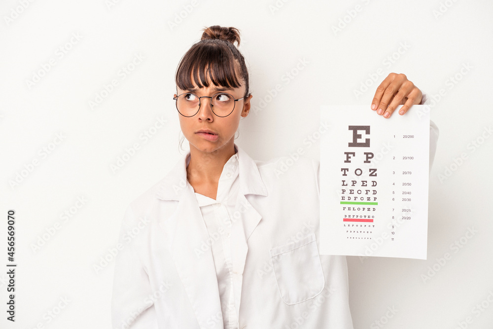 Young mixed race optician woman doing a test isolated on white background confused, feels doubtful and unsure. Young mixed race optician woman doing a test isolated on white background confused, feels doubtful and unsure.
