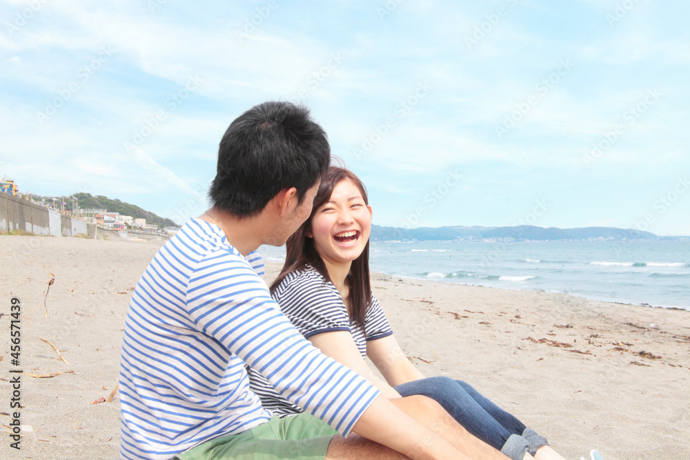 Fototapeta premium Young couple sitting on beach laughing