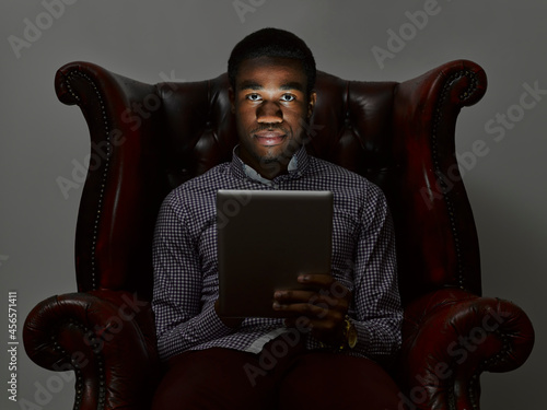Canvas Print Portrait of sinister young man in armchair with digital tablet