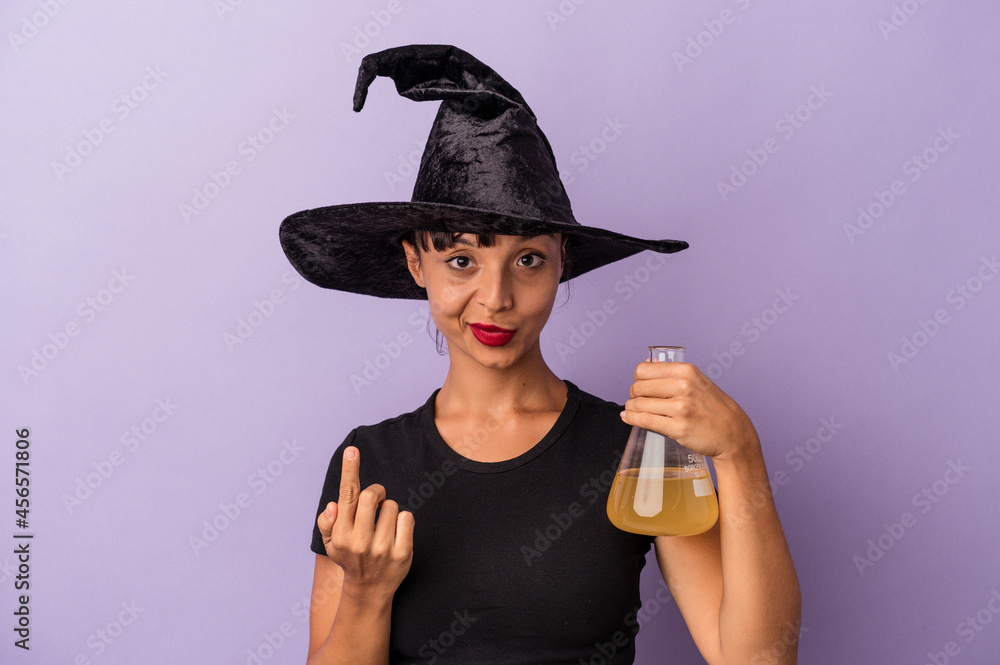 Young mixed race woman disguised as a witch holding potion isolated on purple background  pointing with finger at you as if inviting come closer.