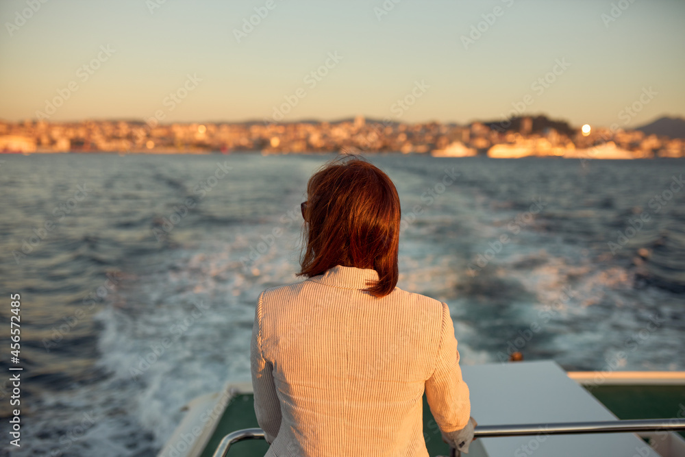 Fototapeta premium Woman with her back on the back of a boat watching as it moves away from the port of the city.