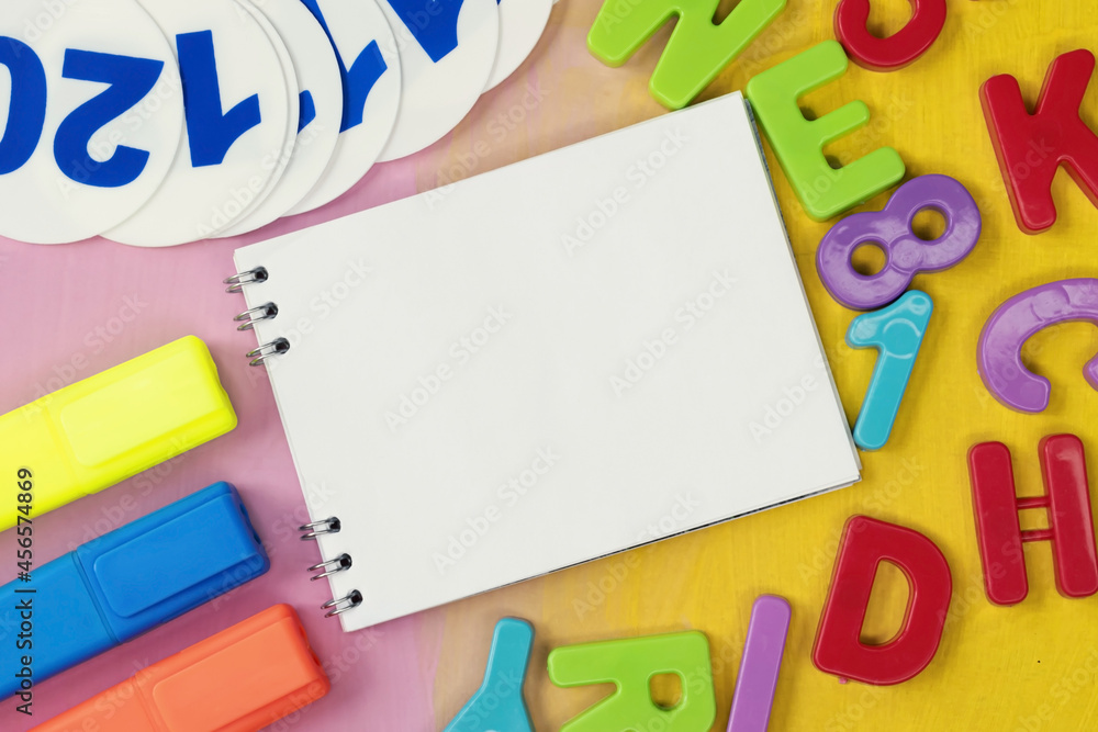 On a painted background among plastic numbers and letters, there is a notebook with a place for text. A marker and a fan of numbers. Educational concept On a painted background among plastic numbers and letters, there is a notebook with a place for text. A marker and a fan of numbers. Educational concept