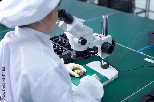 Fototapeta Naklejka Na Ścianę i Meble -  Worker using microscope in factory that specialises in creating functional circuits on flexible surfaces