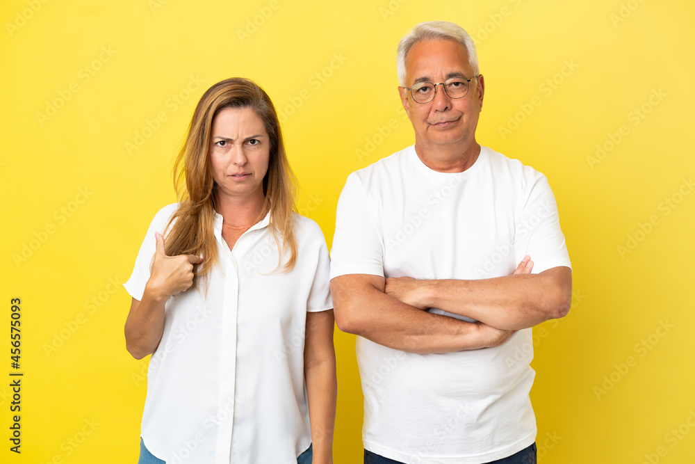 Middle age couple isolated on yellow background annoyed angry in furious gesture Middle age couple isolated on yellow background annoyed angry in furious gesture