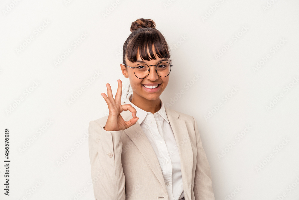 Young mixed race woman isolated on white background winks an eye and holds an okay gesture with hand. Young mixed race woman isolated on white background winks an eye and holds an okay gesture with hand.