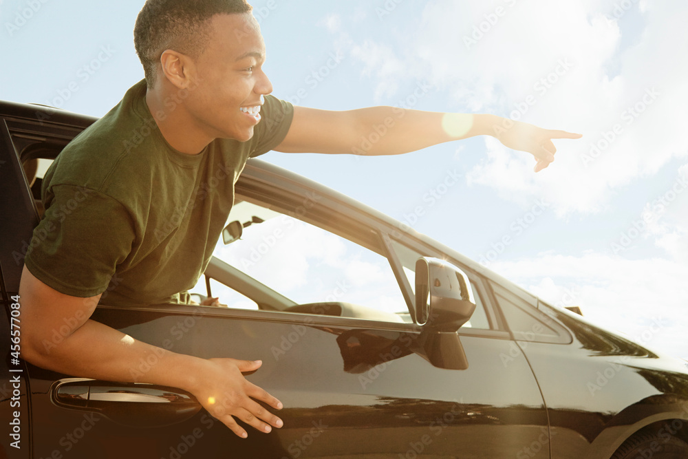 Young man leaning out of car window pointing and smiling