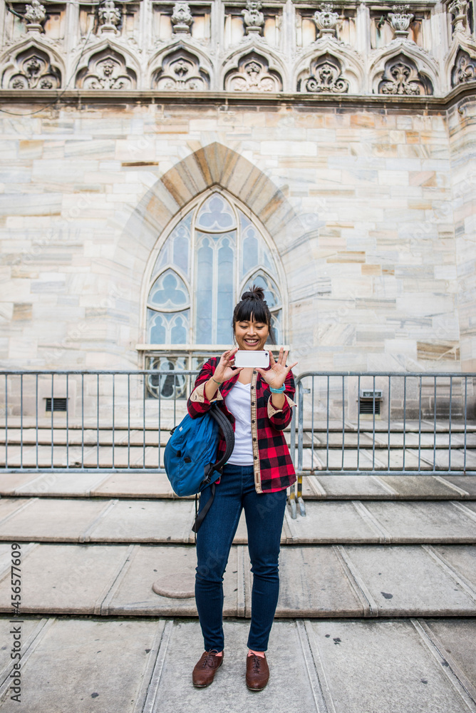 Woman taking selfie in front of Duomo Cathedral, Milan, Italy