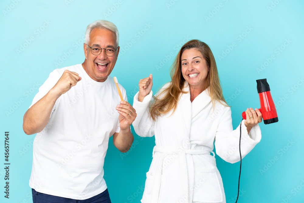 Middle age couple holding dryer and toothbrush isolated on blue background celebrating a victory Middle age couple holding dryer and toothbrush isolated on blue background celebrating a victory