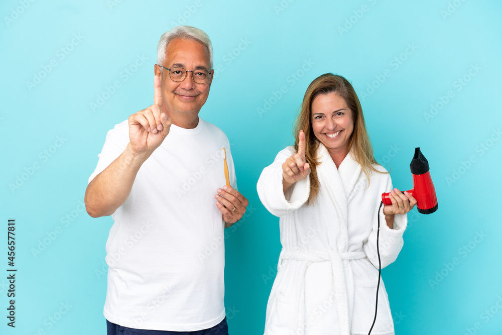 Middle age couple holding dryer and toothbrush isolated on blue background showing and lifting a finger Middle age couple holding dryer and toothbrush isolated on blue background showing and lifting a finger