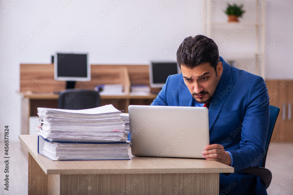 Young male employee unhappy with excessive work at workplace Young male employee unhappy with excessive work at workplace