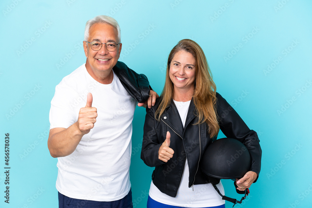 Middle age bikers couple with a motorcycle helmet isolated on blue background giving a thumbs up gesture because something good has happened