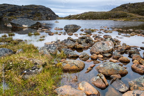 Nunavut landscape - rocks next to a small lake with mountains at the background