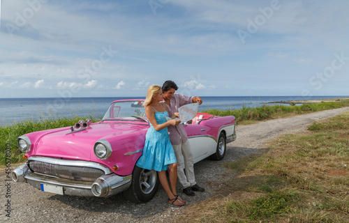 Photography Young couple looking at map beside vintage convertible at coast, Havana, Cuba