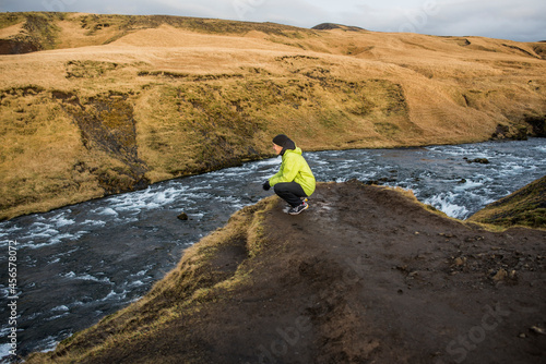 Obraz na plátne Male tourist crouching on riverbank, Skogafoss, Iceland