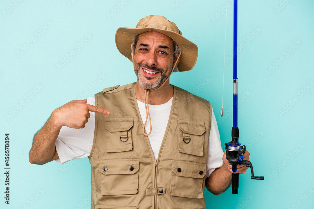 Middle age caucasian fisherman holding rod isolated on blue background person pointing by hand to a shirt copy space, proud and confident Middle age caucasian fisherman holding rod isolated on blue background person pointing by hand to a shirt copy space, proud and confident