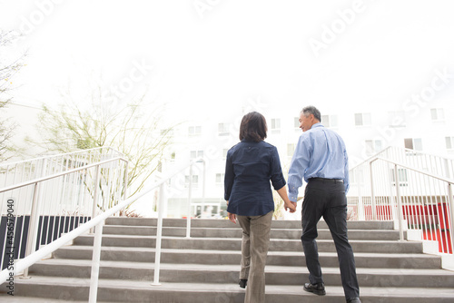 Low angle full length rear view of mature couple holding hands ascending stairs