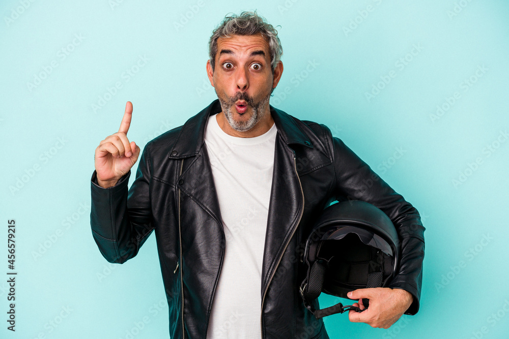 Fototapeta premium Middle age biker caucasian man holding helmet isolated on blue background having some great idea, concept of creativity.