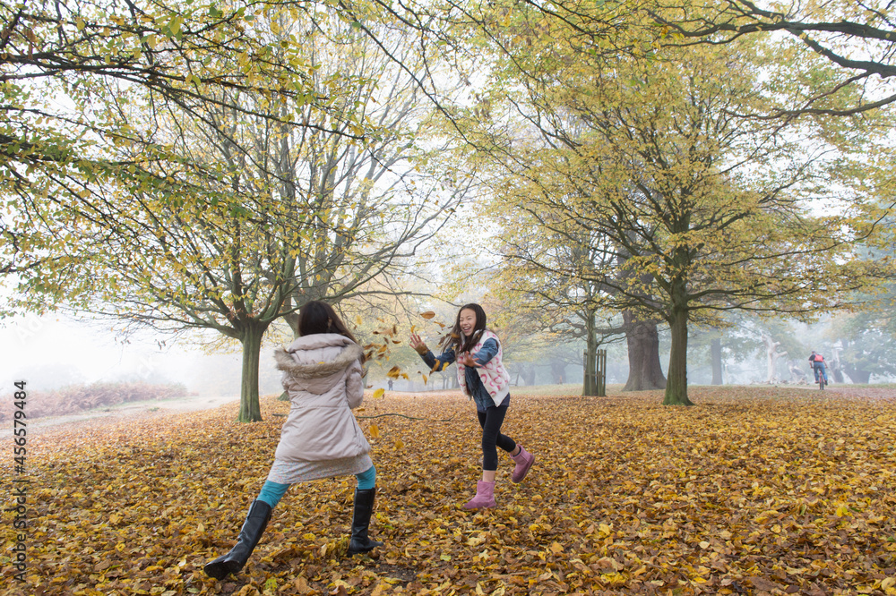 Fototapeta premium Two young girls playing, throwing leaves, in forest, autumn