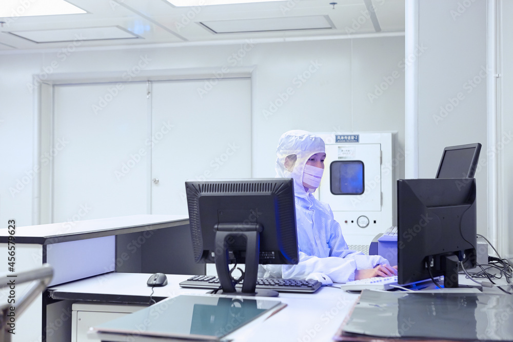 Female factory worker using computer in flexible electronics factory clean room Female factory worker using computer in flexible electronics factory clean room