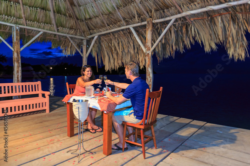 Romantic couple raising a champagne toast at waterfront restaurant, St. Georges Caye, Belize, Central America