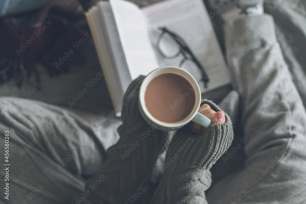 Woman holding cup with cacao or coffee, reading book. Concept of cozy home, comfort leisure Woman holding cup with cacao or coffee, reading book. Concept of cozy home, comfort leisure