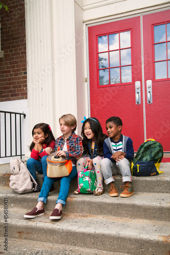 Elementary schoolgirls and boys sitting on elementary school doorway stairs