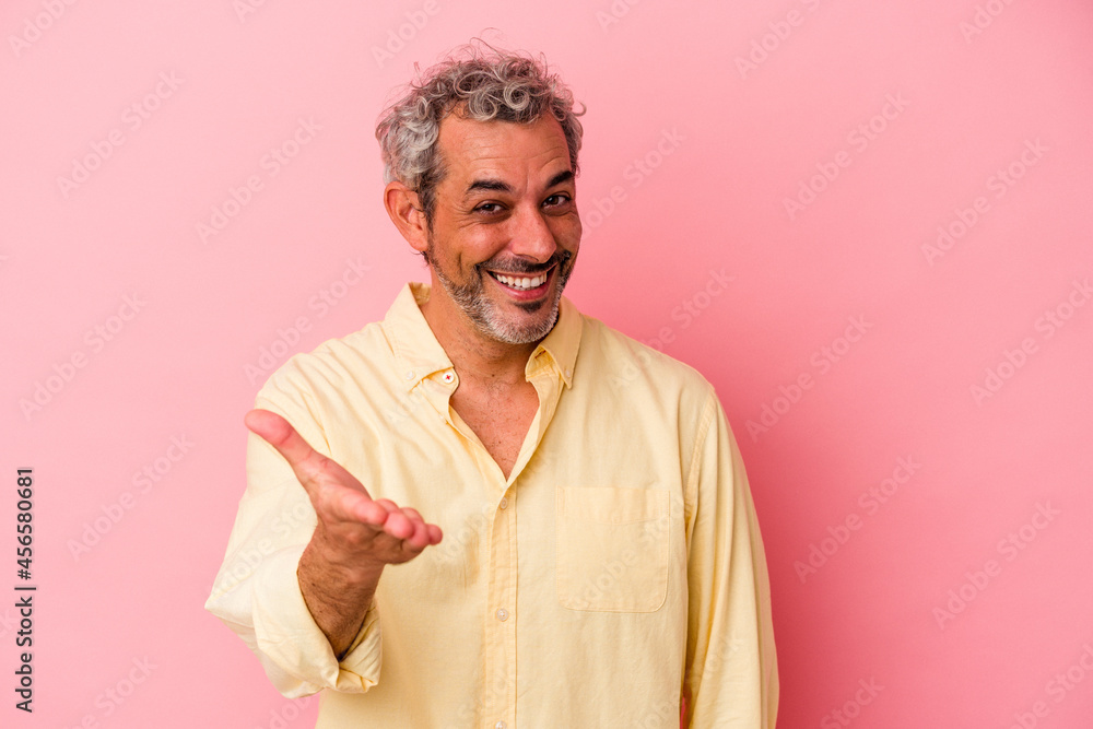 Middle age caucasian man isolated on pink background stretching hand at camera in greeting gesture. Middle age caucasian man isolated on pink background stretching hand at camera in greeting gesture.