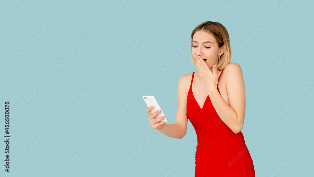 Online communication. Amazed woman. Digital life. Advertising background. Pretty surprised lady looking on smartphone screen isolated blue copy space. Online communication. Amazed woman. Digital life. Advertising background. Pretty surprised lady looking on smartphone screen isolated blue copy space.