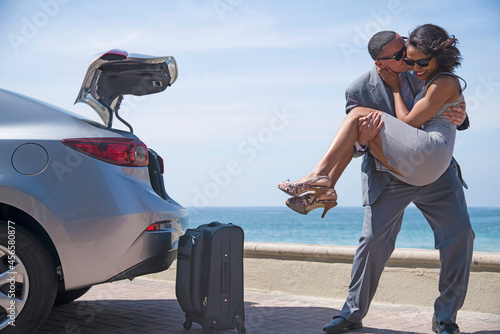 Man kissing woman in arms beside luggage on beach
