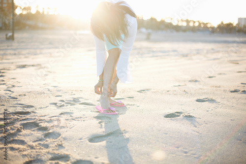 Woman bending to fasten anklet on Santa Monica beach, California, USA photo