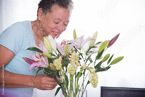 Senior woman smelling vase of flowers, smiling photo