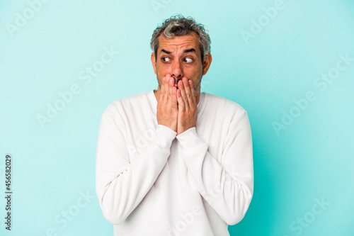 Middle age caucasian man isolated on blue background thoughtful looking to a copy space covering mouth with hand.