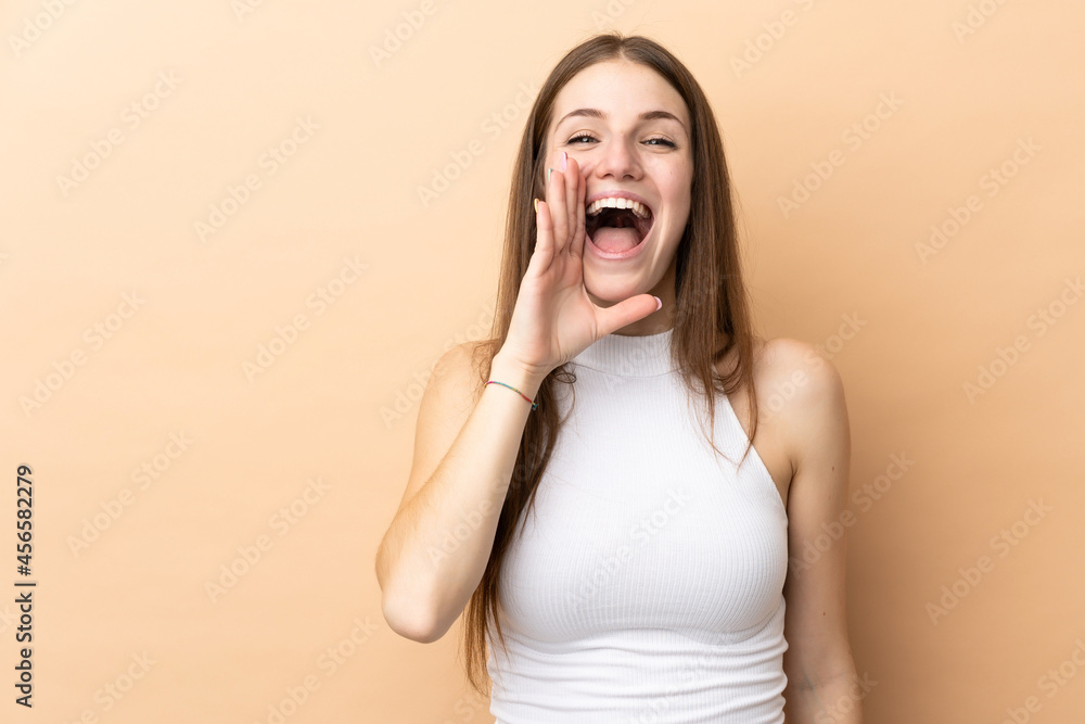 Young caucasian woman isolated on beige background shouting with mouth wide open Young caucasian woman isolated on beige background shouting with mouth wide open