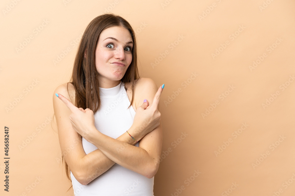 Obraz premium Young caucasian woman isolated on beige background pointing to the laterals having doubts