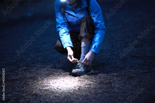 Female hiker wearing head torch tying hiking boot laces at night