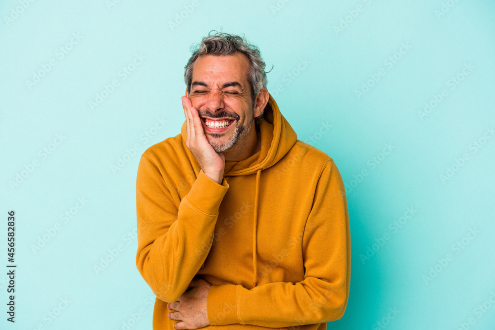 Middle age caucasian man isolated on blue background laughs happily and has fun keeping hands on stomach. Middle age caucasian man isolated on blue background laughs happily and has fun keeping hands on stomach.