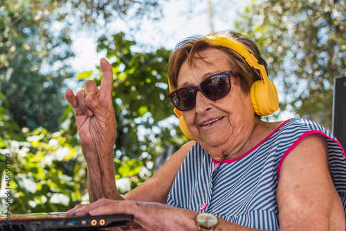elderly woman with sunglasses and headphones raises two fingers in horns