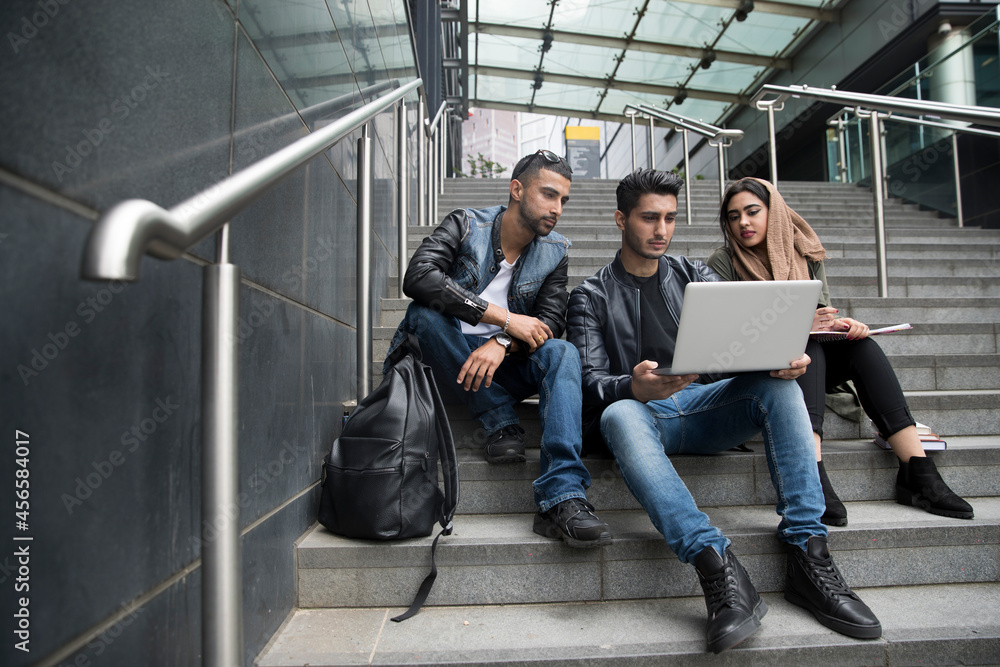 Three friends, sitting on steps, looking at laptop