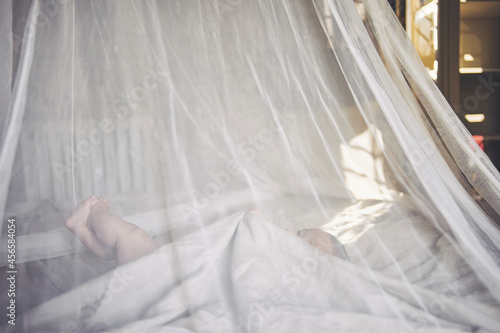 Baby girl lying in net draped crib grasping bed sheet © Cultura Allies
