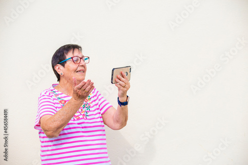 mujer mayor sonrie saluda con la mano videollamada con telefono movil aislada en fondo amarillo photo