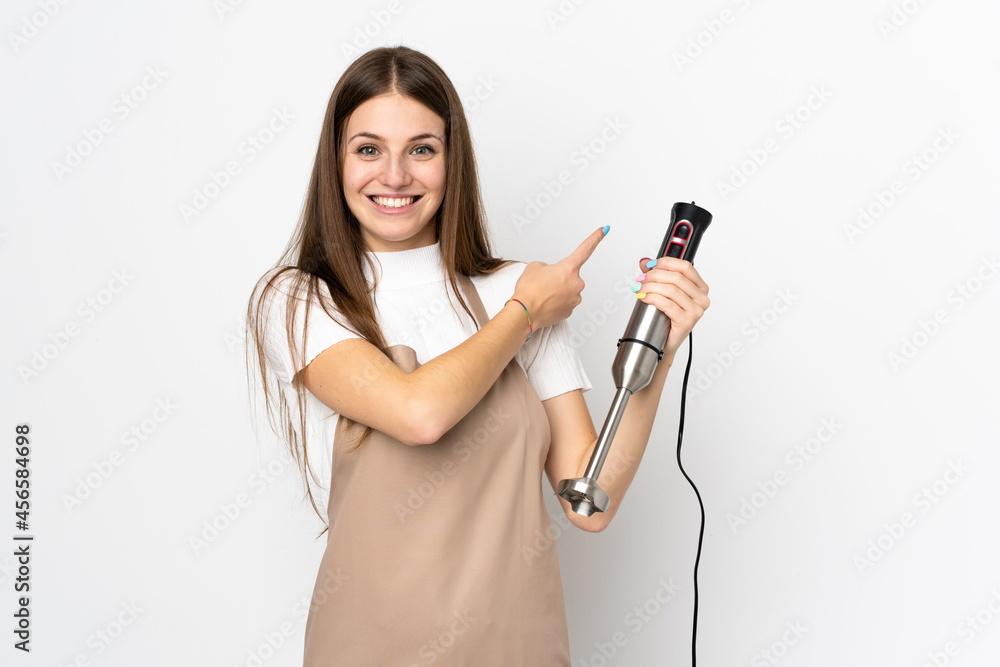 Young woman using hand blender isolated on white background pointing finger to the side Young woman using hand blender isolated on white background pointing finger to the side