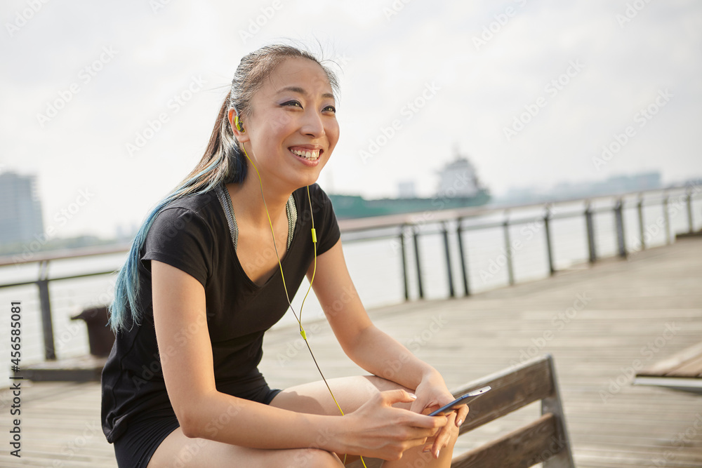 Woman wearing earphones holding smartphone smiling Woman wearing earphones holding smartphone smiling