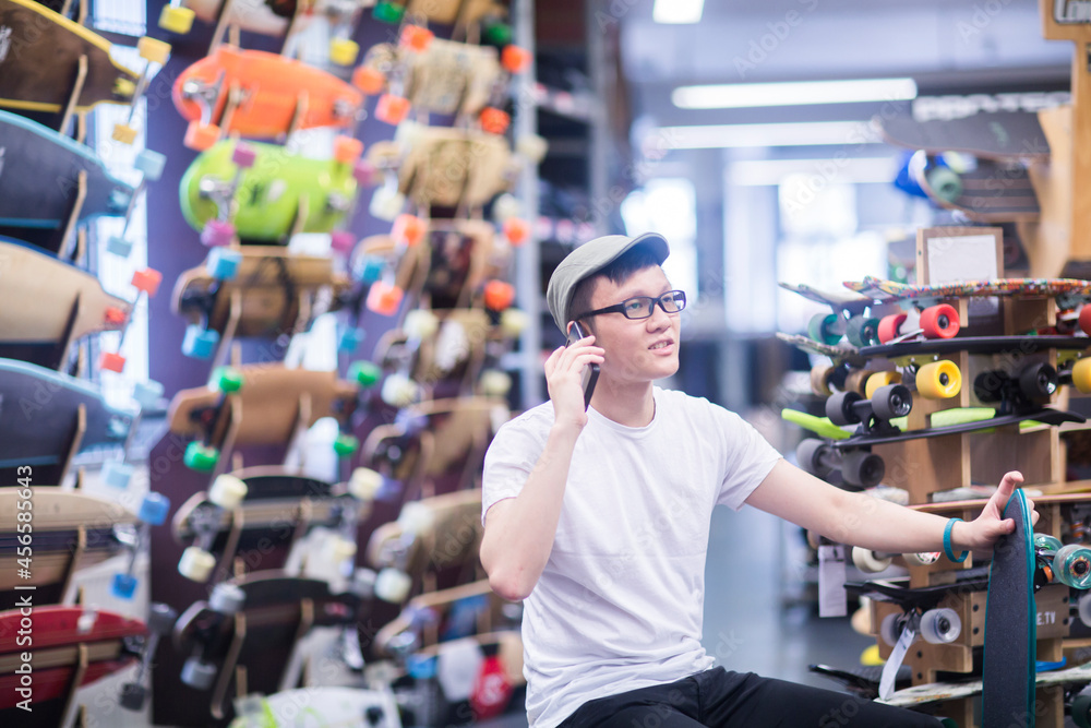 Young male skateboarder making smartphone call in skateboard shop